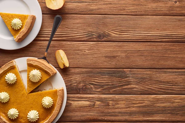 茶色の木製テーブルの上にアップルカットの近くにホイップクリームとおいしいカボチャパイ — ストック写真
