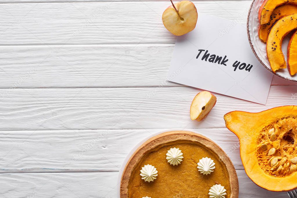 top view of pumpkin pie, ripe apples and thank you card on wooden white table