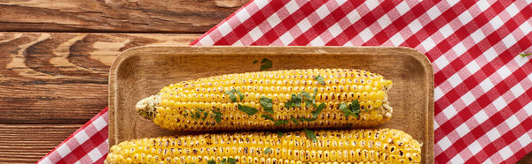 top view of grilled corn served on red checkered napkin at wooden table for Thanksgiving dinner, panoramic shot