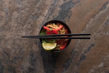 top view of delicious spicy thai noodles with chopsticks in bowl on stone surface clipart
