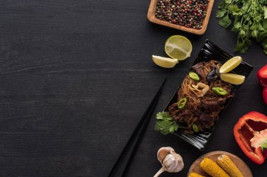 Yemek çubuklarının yanındaki lezzetli Tayland eriştelerinin ve ahşap gri yüzeydeki taze malzemelerin üst görüntüsü.