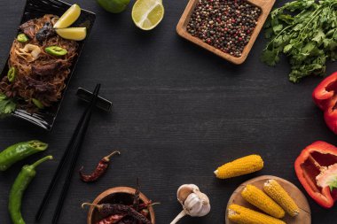 Yemek çubuklarının yanındaki lezzetli Tayland eriştelerinin ve ahşap gri yüzeydeki taze malzemelerin üst görüntüsü.