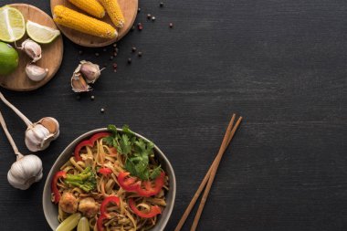 top view of tasty spicy thai noodles with shrimps near chopsticks and fresh ingredients on wooden grey surface with copy space clipart