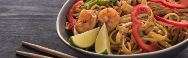 close up view of thai noodles with shrimps near chopsticks on wooden grey surface, panoramic shot clipart
