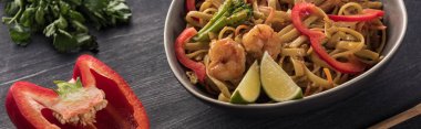 close up view of thai noodles with shrimps near parsley and bell pepper on wooden grey surface, panoramic shot clipart
