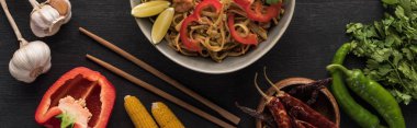 top view of tasty spicy thai noodles with garlic, parsley, corn, bell pepper, jalapenos near chopsticks on wooden grey surface, panoramic shot clipart