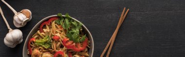 top view of tasty spicy thai noodles with garlic near chopsticks on wooden grey surface, panoramic shot clipart