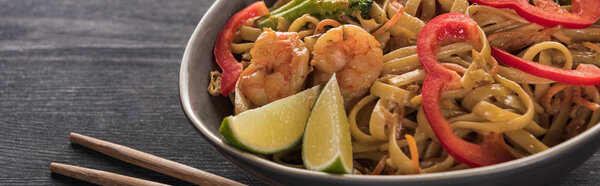 close up view of thai noodles with shrimps near chopsticks on wooden grey surface, panoramic shot