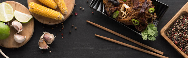 top view of tasty spicy thai noodles near chopsticks and fresh ingredients on wooden grey surface, panoramic shot