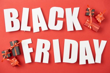 top view of black friday white lettering near small presents on red background clipart
