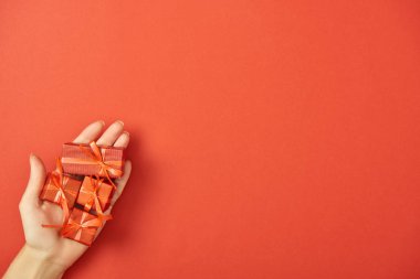 Elinde dekoratif hediye kutularıyla kırmızı arka planda fotokopi alanı olan bir kadının kısmi görünümü