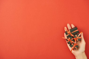 Elinde dekoratif siyah hediye kutularıyla kırmızı arka planda fotokopi alanı olan bir kadının kısmi görünümü