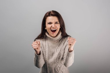 excited woman in sweater showing yes gesture isolated on grey  clipart