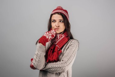 pensive woman in red knitted had, gloves and scarf isolated on grey  clipart