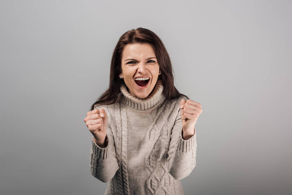 excited woman in sweater showing yes gesture isolated on grey 