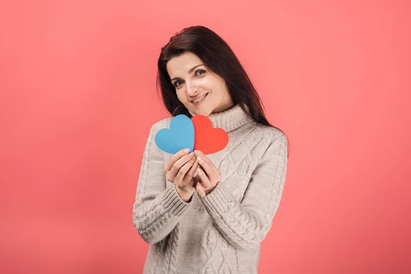 Happy woman in sweater holding blue and red heart-shaped paper artwork on pink — Stock Image Happy Woman Sweater Holding Blue Red Heart Shaped Paper Artwork Stock Picture