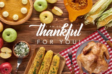 top view of pumpkin pie, turkey and vegetables served at wooden table with i am so thankful for you illustration clipart