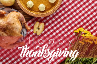 Kabak turtası ve kırmızı kareli peçetede kızarmış hindi ve sarı çiçekler ve mutlu şükran günü çizimleri.