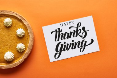 top view of pumpkin pie and card with happy thanksgiving illustration on orange background clipart