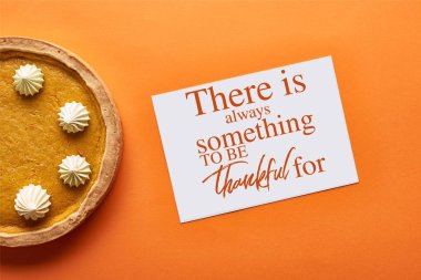 top view of pumpkin pie and card with there is always something to be thankful for illustration on orange background