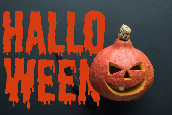 top view of carved spooky Halloween pumpkin with knife on black background with bloody Halloween lettering