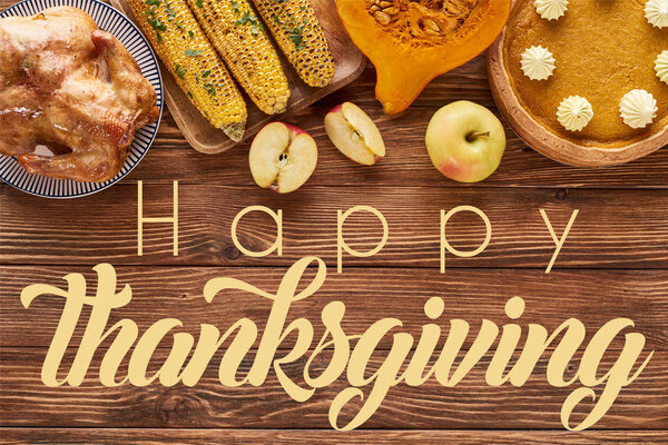 вид сверху на тыквенный пирог, индейку и овощи, подаваемые за деревянным столом с счастливой иллюстрацией к Дню благодарения
