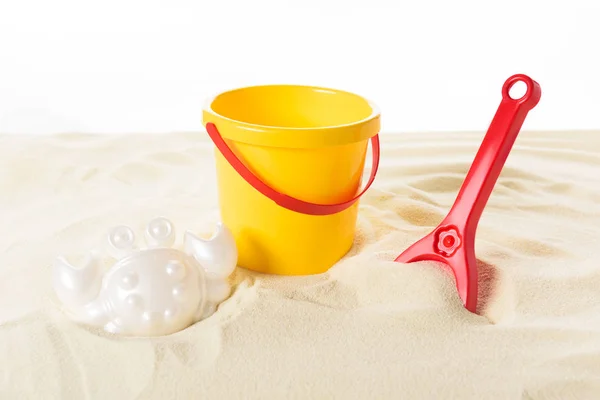 Cubo y juguetes de plástico en arena aislada en blanco - foto de stock