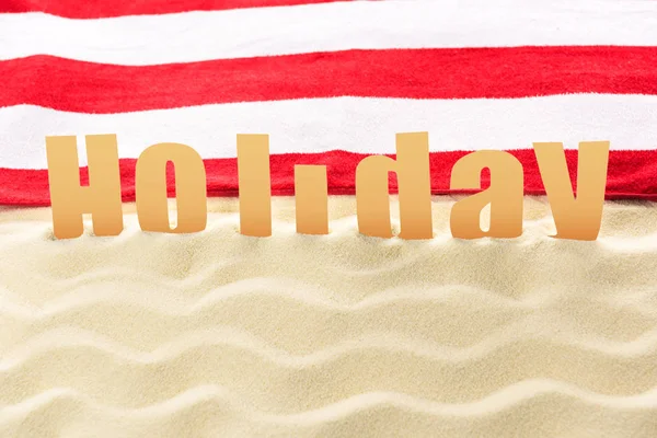 Holiday inscription in front of towel on sandy beach — Stock Photo