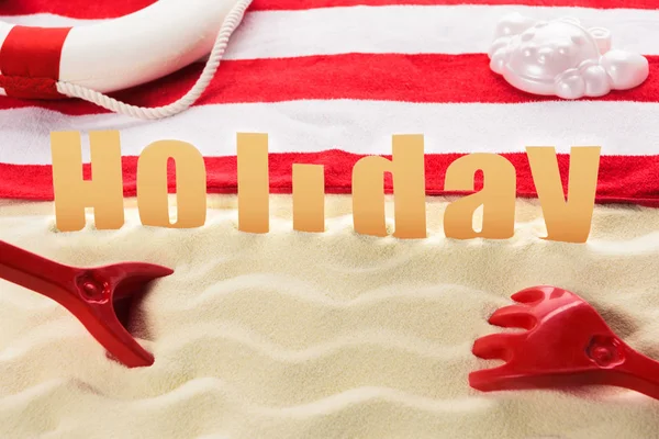 Beach toys and towel with Holiday inscription on sandy beach — Stock Photo