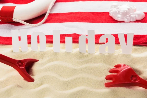 Juguetes de playa y toalla con palabra Vacaciones en playa de arena - foto de stock