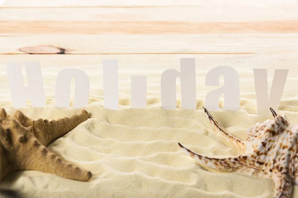 Stella marina con conchiglia e iscrizione Holiday sulla spiaggia di sabbia — Foto stock