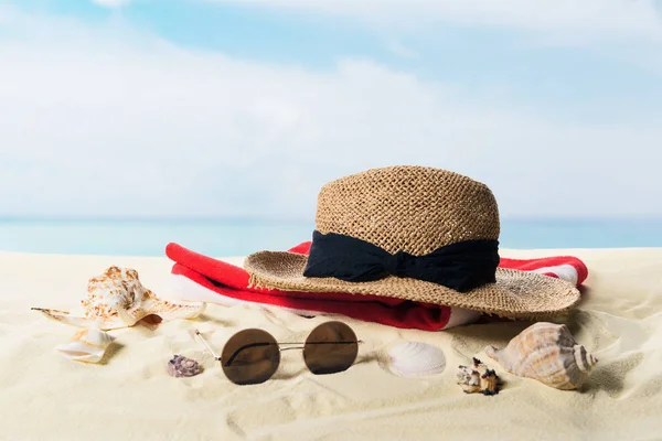 Sombrero de paja y gafas de sol con conchas marinas en arena sobre fondo azul cielo - foto de stock