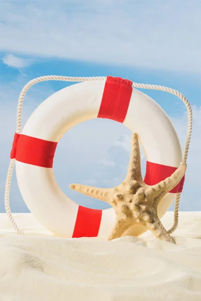 Life ring and starfish in sand on blue sky background — Stock Photo