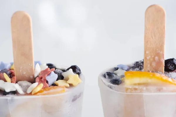 Close-up view of sweet homemade ice cream with sticks in containers on grey — Stock Photo