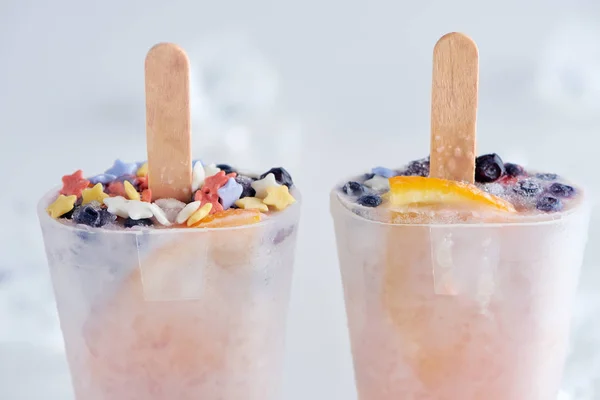 Крупный план вкусного домашнего мороженого с палочками в контейнерах на сером — стоковое фото