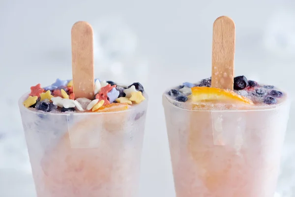 Close-up view of tasty homemade ice cream with sticks in containers on grey — Stock Photo