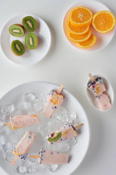 Top view of delicious homemade popsicles with ice cubes and sliced kiwi and orange on grey — Stock Photo