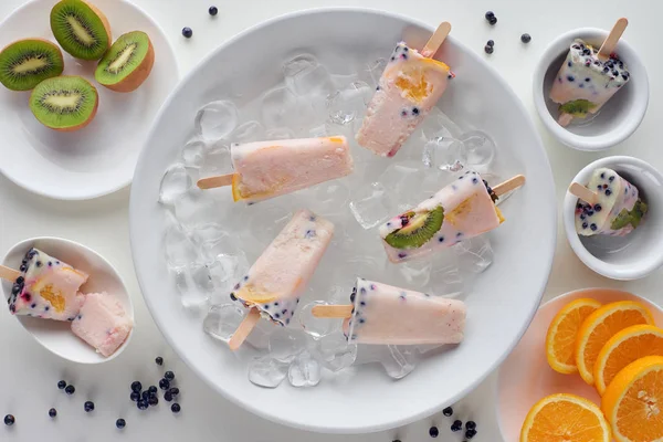 Top view of delicious homemade popsicles with ice cubes and sliced fruits on grey — Stock Photo