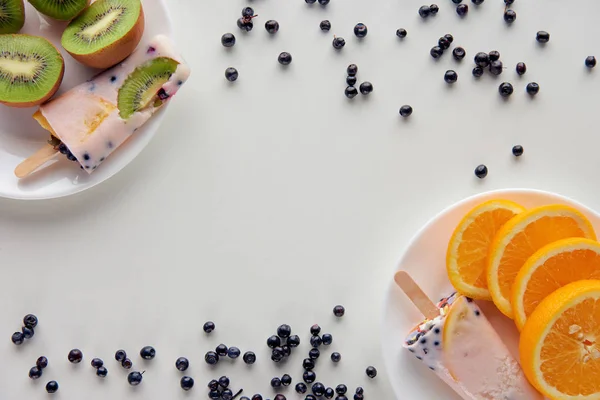 Vista superior de saborosos picolés caseiros com fatias de laranja e kiwi em pratos e bagas em fundo cinza — Fotografia de Stock