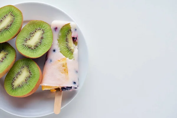 Vue de dessus de délicieuse popsicle maison avec des baies et des tranches de kiwi sur assiette sur gris — Photo de stock