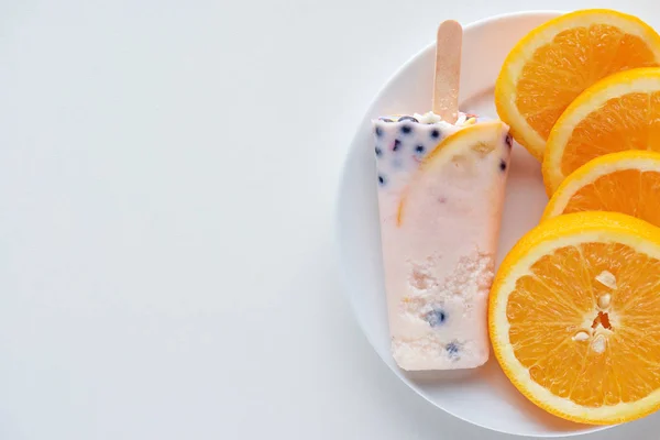 Blick von oben auf köstliches hausgemachtes Eis am Stiel mit Beeren und Orangenscheiben auf Teller auf grau — Stockfoto