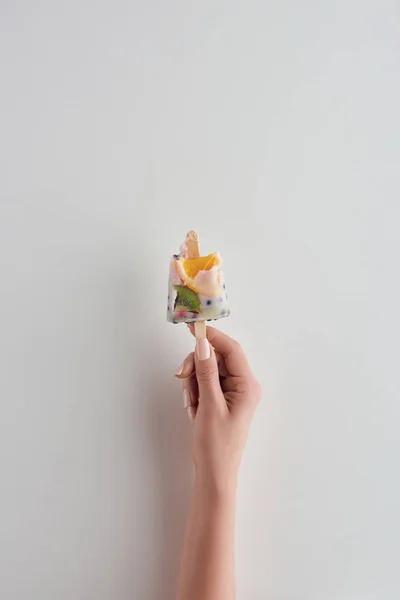 Cropped shot of person holding fresh cold fruity popsicle on stick on grey — Stock Photo