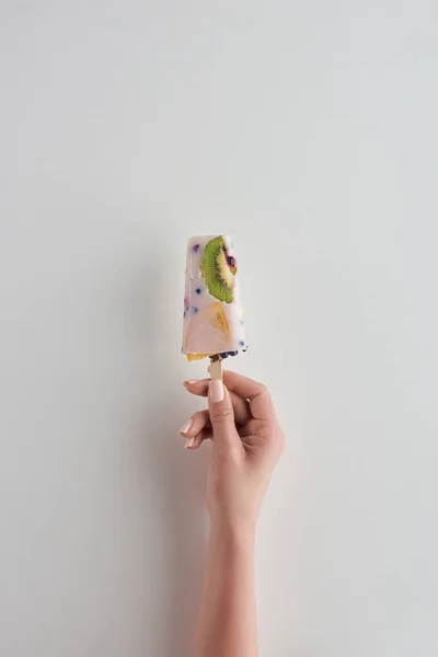 Cropped shot of person holding fresh cold fruity popsicle on grey — Stock Photo