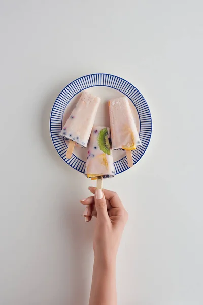 Tiro recortado de la persona que sostiene delicioso paleta afrutada por encima del plato en gris — Stock Photo