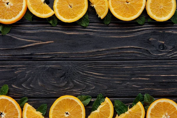 Вид зверху зі свіжих апельсинових скибочок і листя м'яти на темній дерев'яній стільниці — стокове фото