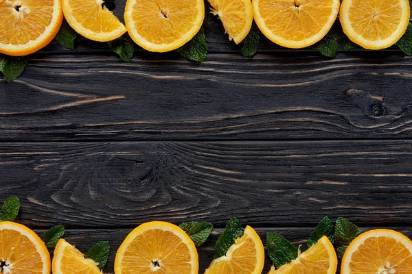 Vue de dessus des tranches d'orange fraîches et des feuilles de menthe sur le dessus de table en bois foncé — Photo de stock