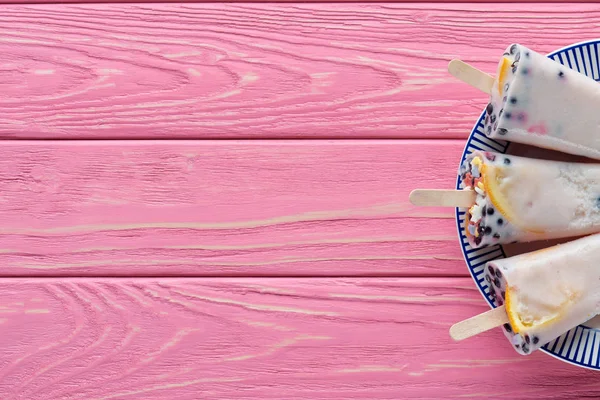 Blick von oben auf süße leckere hausgemachte Eis am Stiel mit Früchten und Beeren auf Teller auf rosa Holztisch — Stockfoto