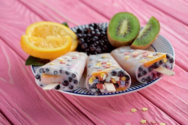 Glace maison sucrée avec des fruits frais et des baies sur assiette sur table en bois rose — Photo de stock