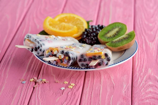 Vista de cerca de paletas caseras con frutas frescas y bayas en el plato en la mesa de madera rosa - foto de stock