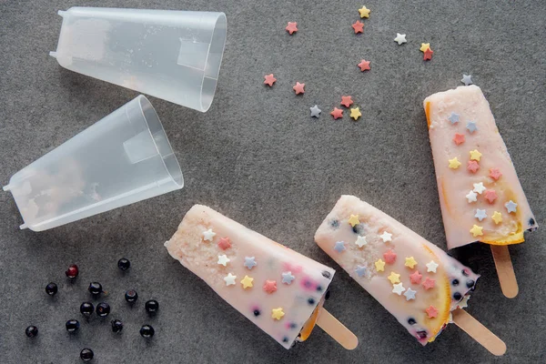 Vista dall'alto di ghiaccioli fruttati freddi dolci, stelle colorate e bacche su grigio — Foto stock